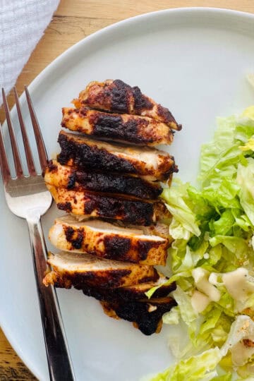 baked boneless skinless chicken thigh cut into strips on a white plate with a Caesar salad.