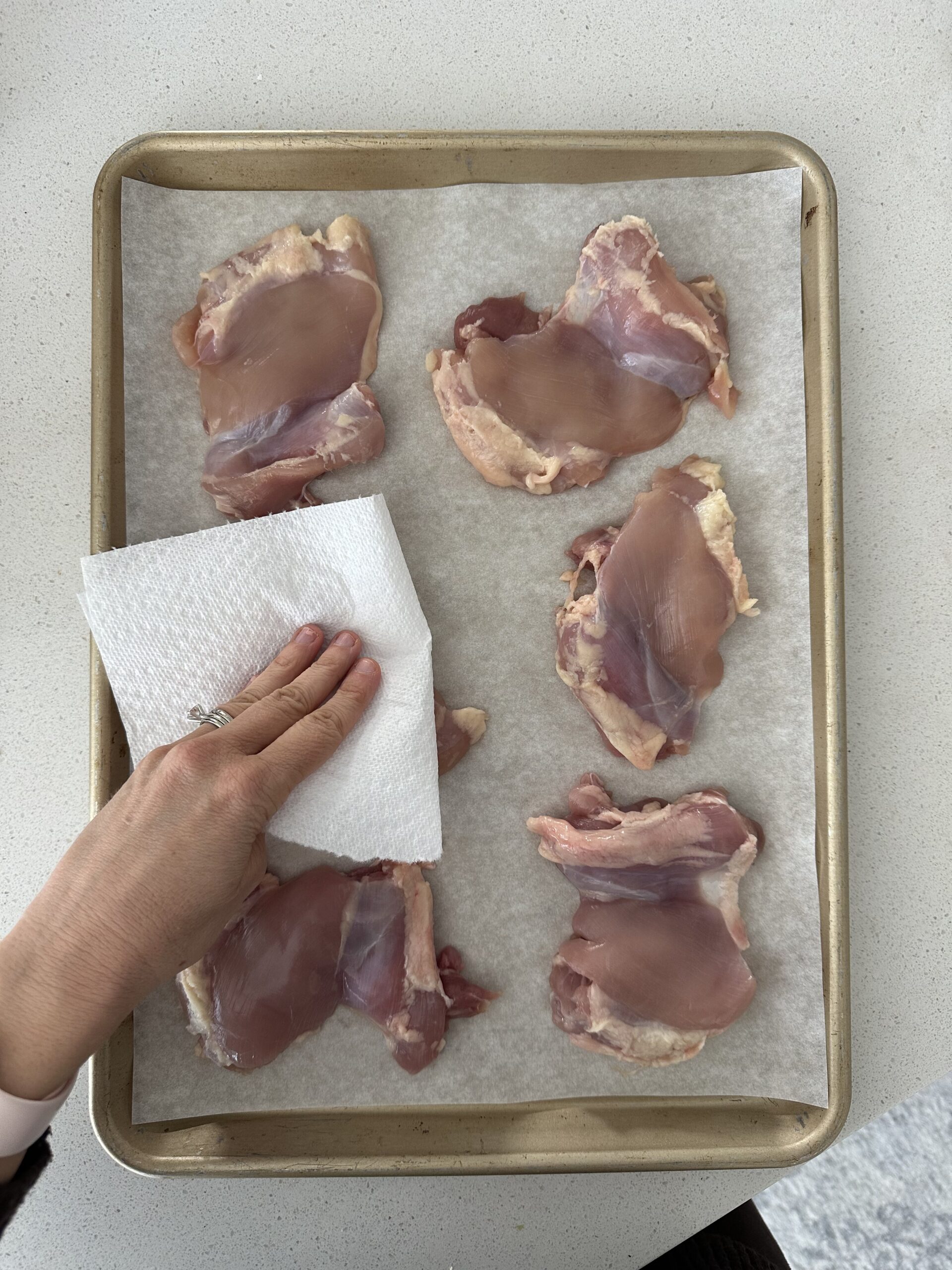 Sheet pan of thighs being patted down with a paper towel.