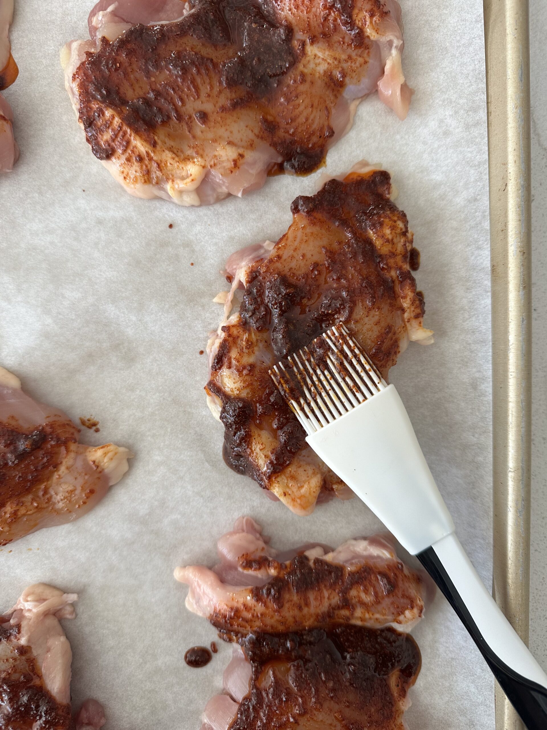 Chicken thighs being brushed with the seasoning mixture.