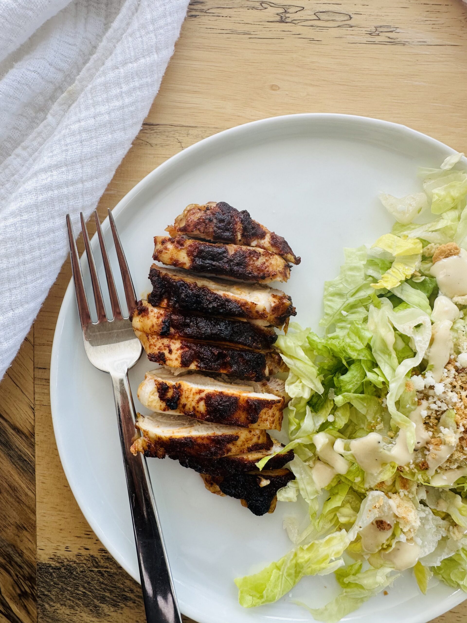 Baked boneless skinless chicken thigh on white plate with Caesar salad.