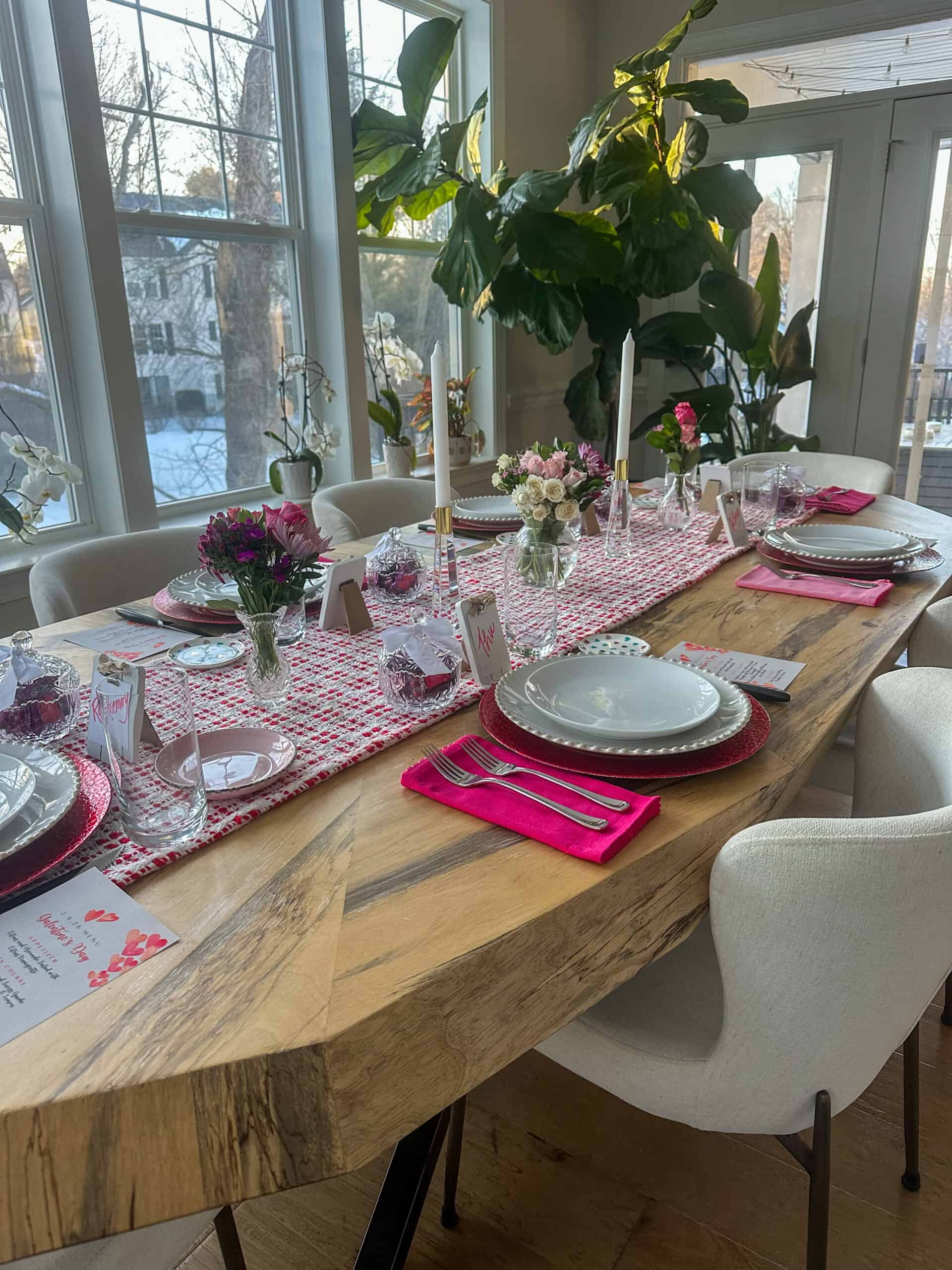 table set for a Galentine's Day brunch, with white plates, pink napkins, and fresh flowers and candles.