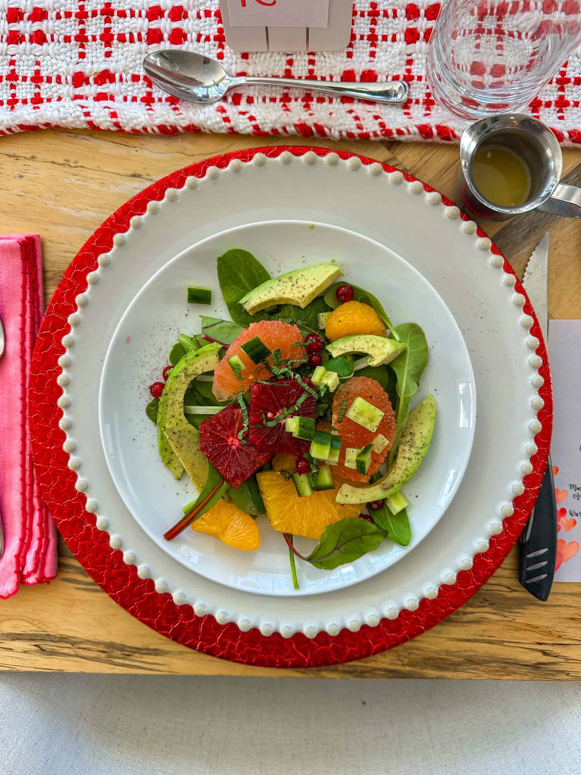 Citrus and avocado salad on a white plate on top of another white plate with a red charger.
