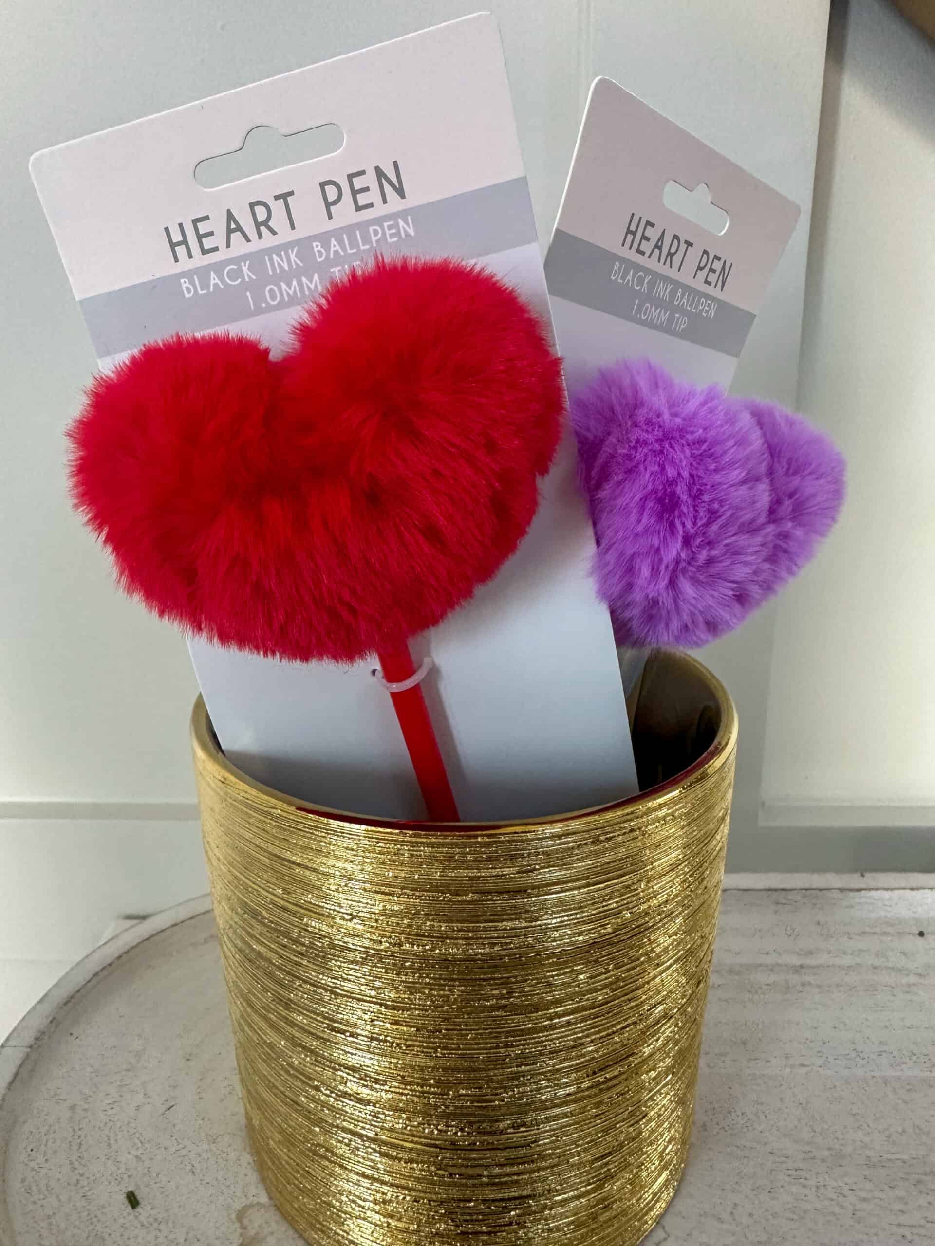 Purple and red fluffy heart pens that were used as favors resting in a gold vase.
