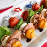 close up of skewers with watermelon, prosciutto, basil, mozzarella, and cataloupe drizzled with balsamic glaze.