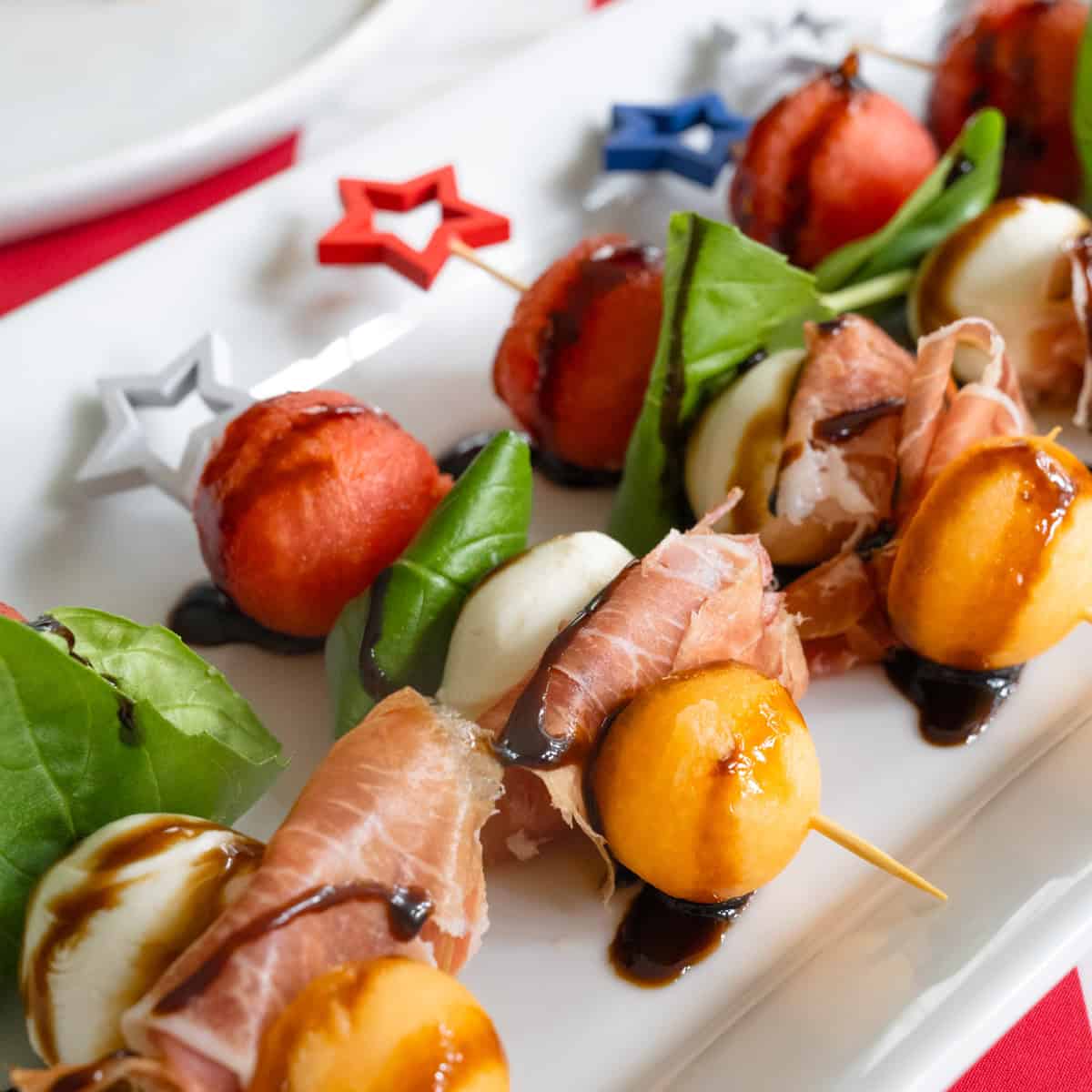 close up of melon and prosciutto skewers on a white tray.