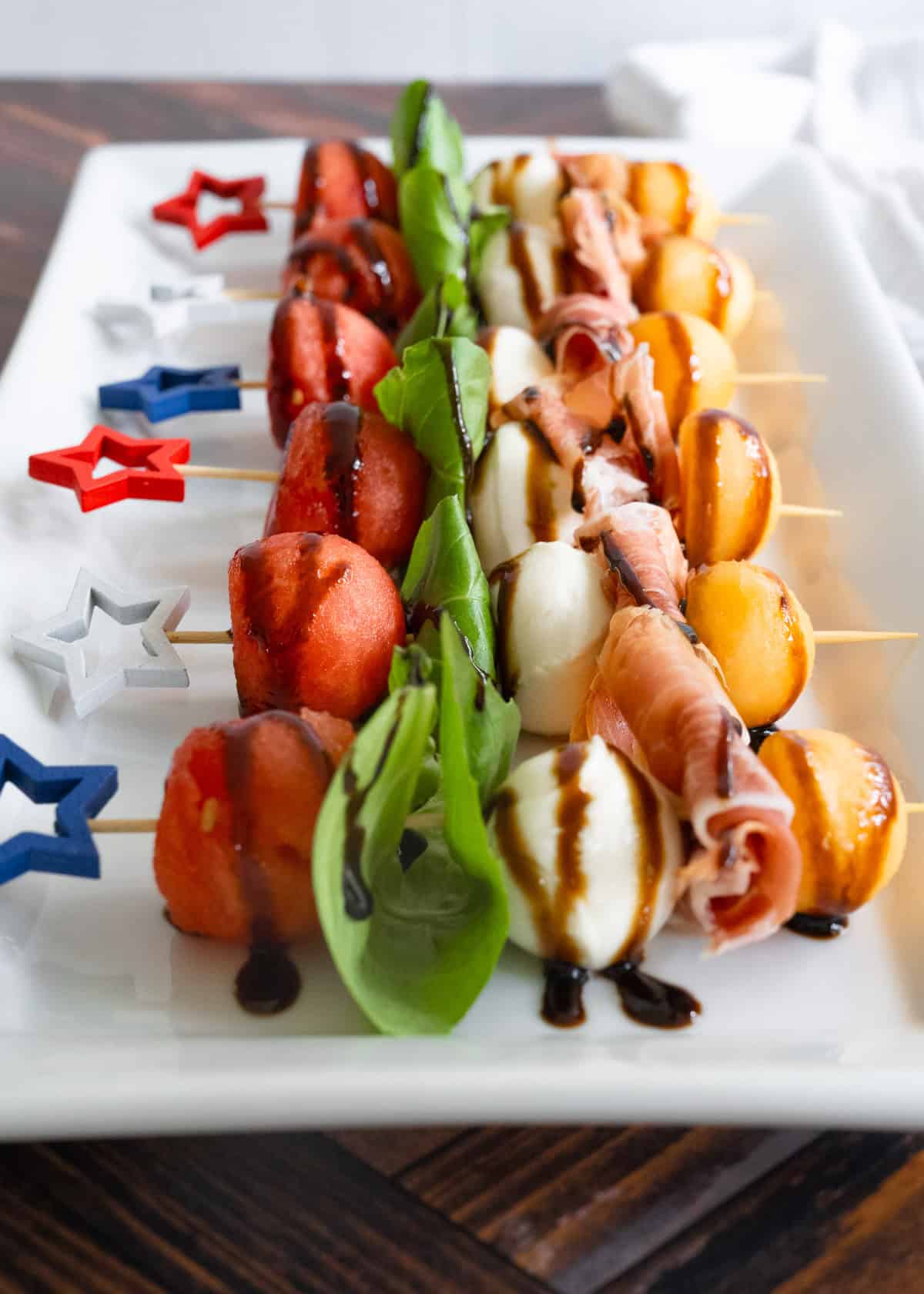 A row of melon, mozzarella, basil, and prosciutto on red, white, and blue star skewers.