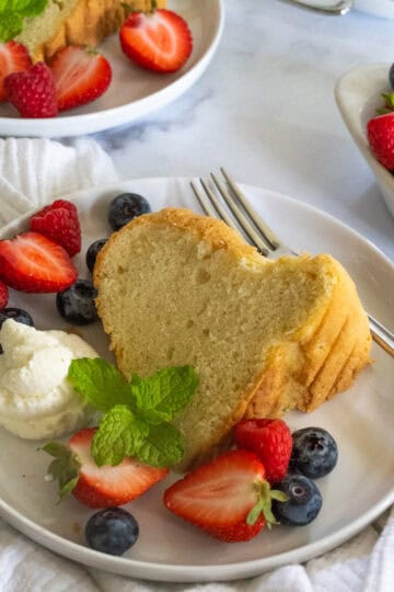 Slice of chiffon cake on a white plate next to a dollop of whipped cream and fresh berries.