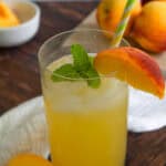 Tall glass of peach lemonade with a peach slice and fresh mint on the rim.