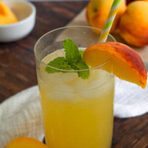 Tall glass of peach lemonade with a peach slice and fresh mint on the rim.