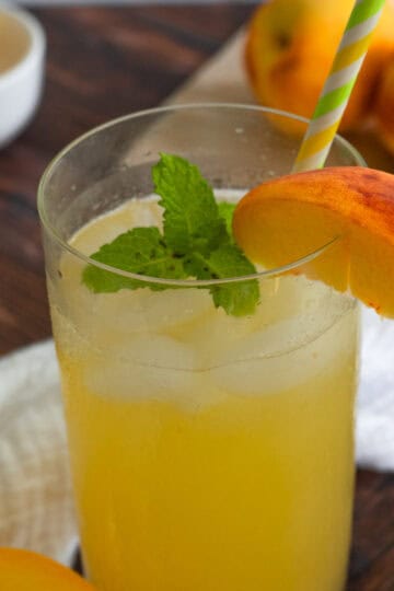 Tall glass of peach lemonade with a peach slice and fresh mint on the rim.
