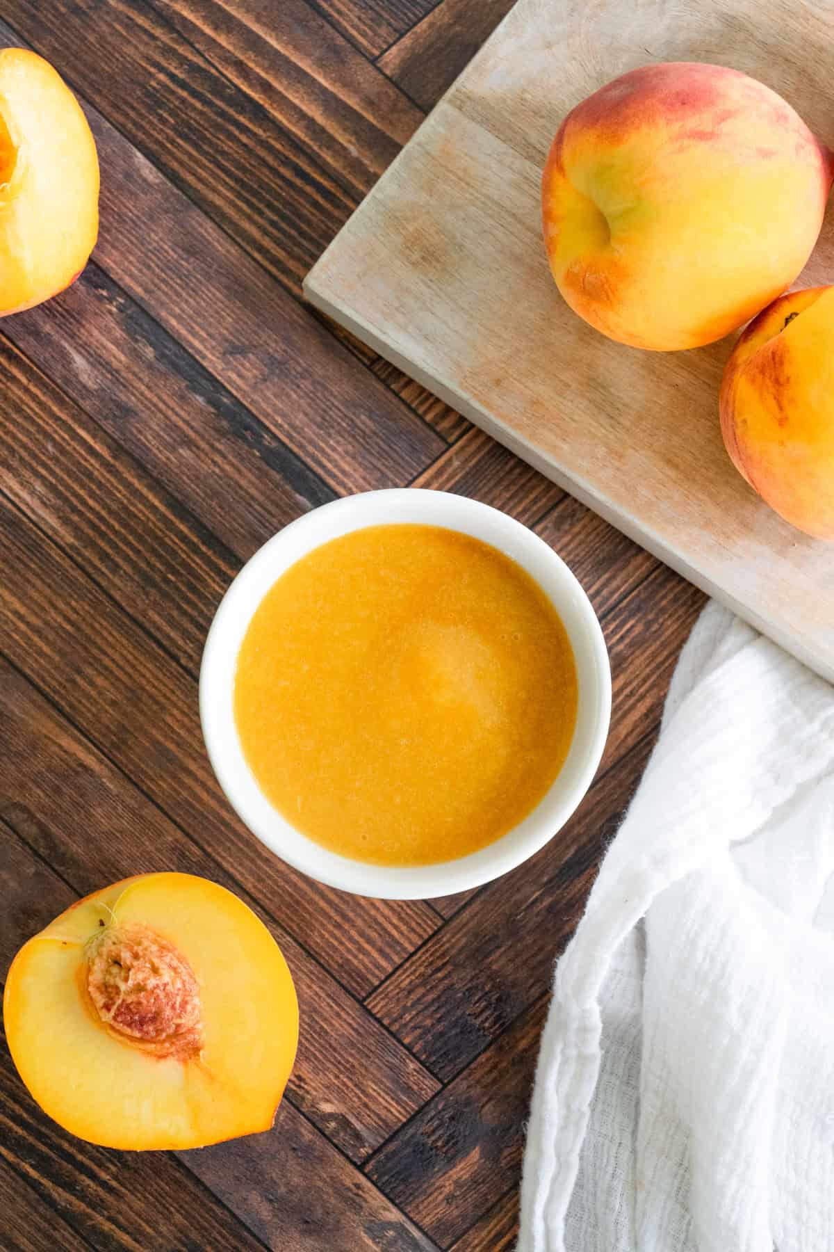 Overhead picture o peaches on a cutting board and a white bowl of pureed peach.