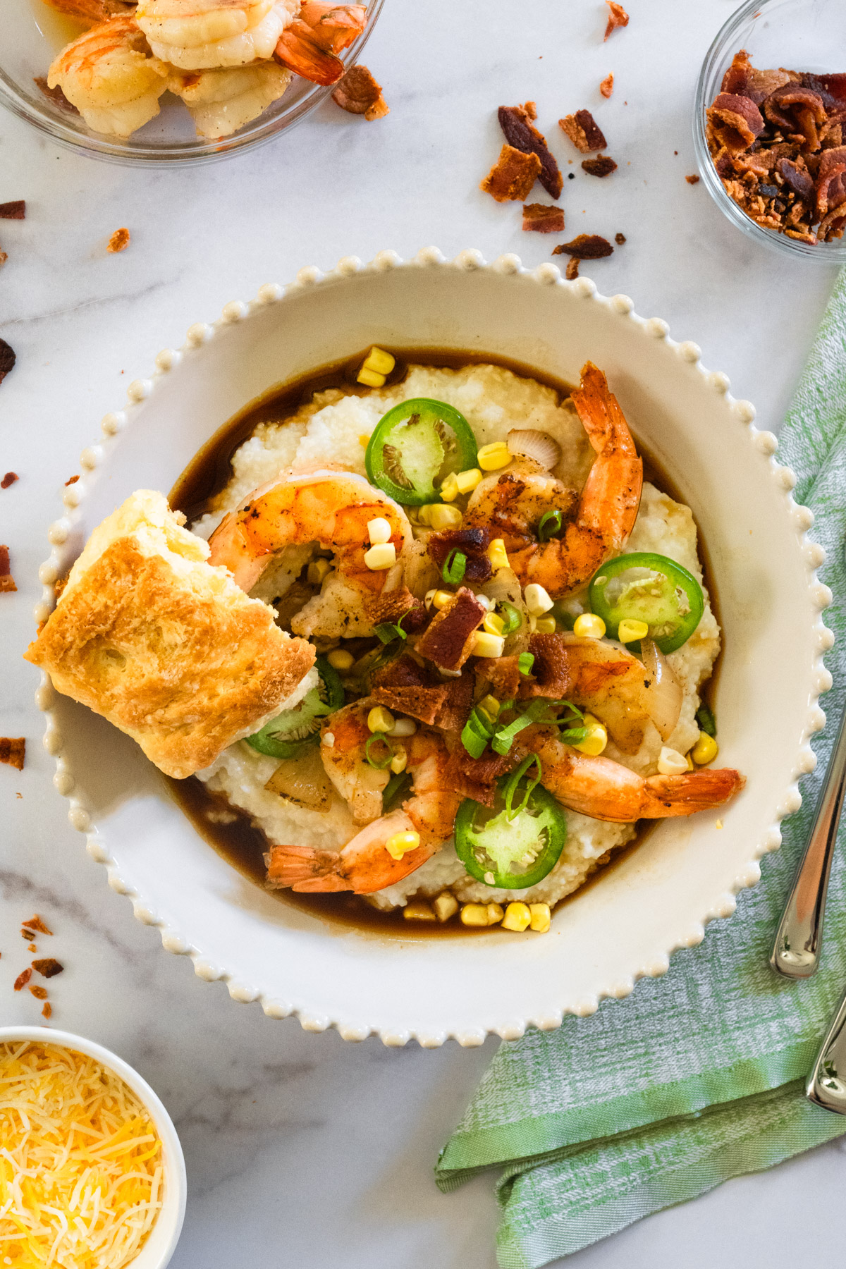 Large bowl of shrimp and grits with a buttermilk biscuit resting on top and extra bacon and shrimp around the bowl.