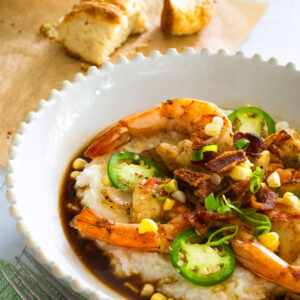 Bowl of Southern Shrimp and Grits with buttermilk biscuits on parchment paper in the background