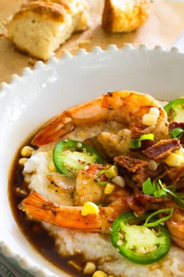 Bowl of Southern Shrimp and Grits with buttermilk biscuits on parchment paper in the background