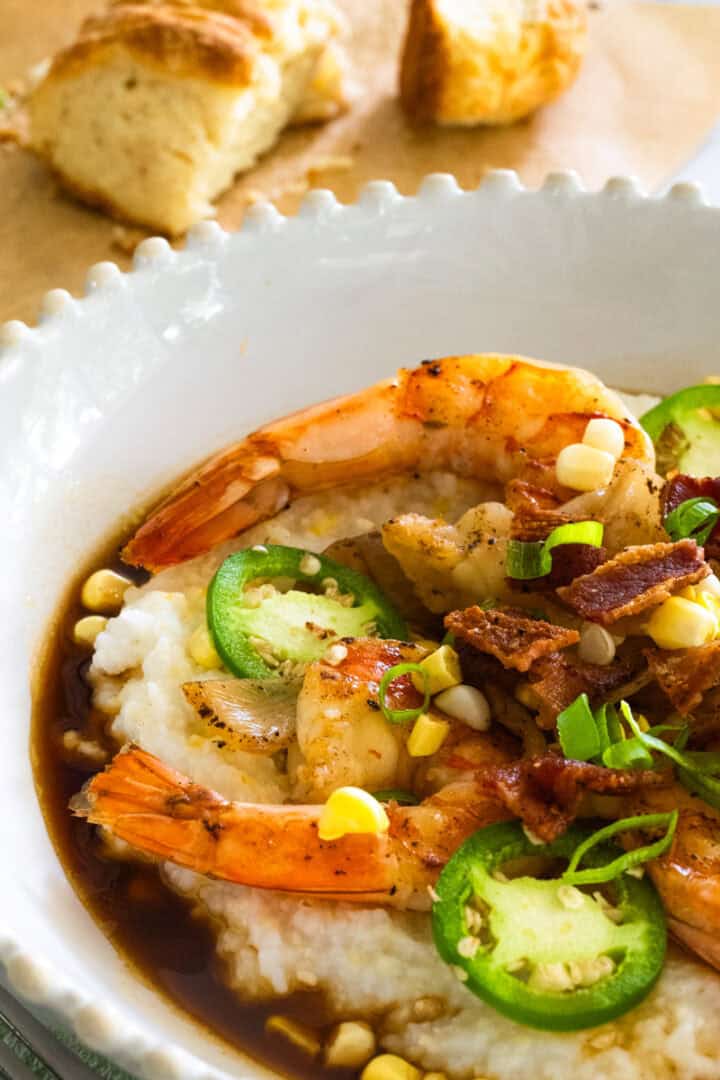 Bowl of Southern Shrimp and Grits with buttermilk biscuits on parchment paper in the background